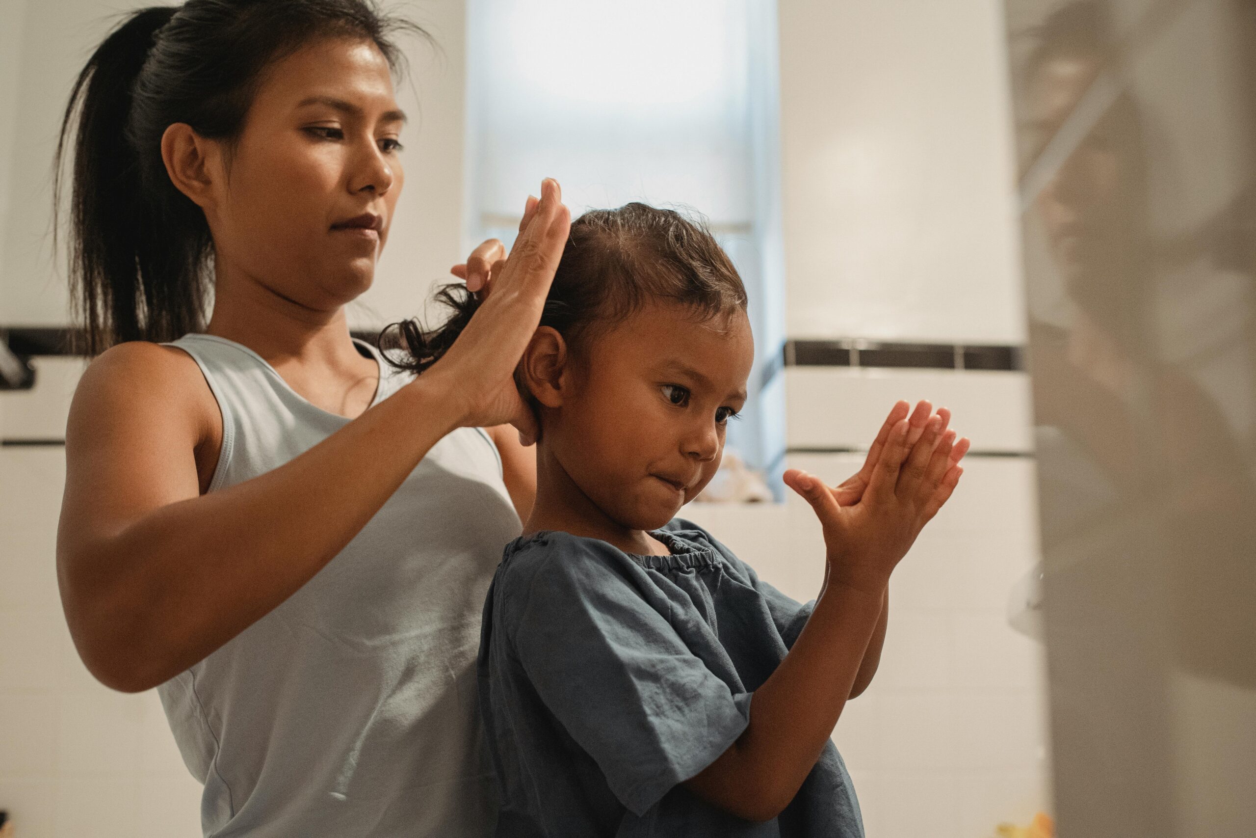 Side view of focused young Hispanic mother braiding hair of cute little girl